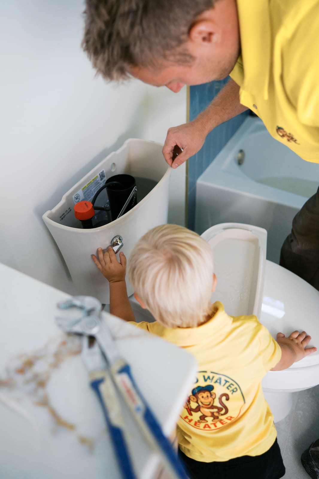 Josh repairing a toilet tank while his son watches